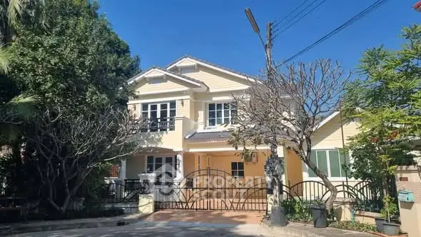 Charming two-story yellow house with lush greenery and gated entrance in a serene neighborhood.