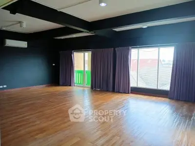Spacious room with wooden flooring and large windows offering natural light.
