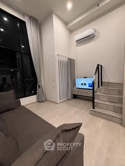 Modern living room with high ceiling, large windows, and staircase leading to mezzanine.