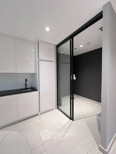 Modern kitchen with sleek white cabinets and black countertop, featuring a sliding glass door to a cozy room.