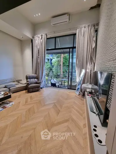 Spacious living room with elegant parquet flooring and large windows opening to a garden view.