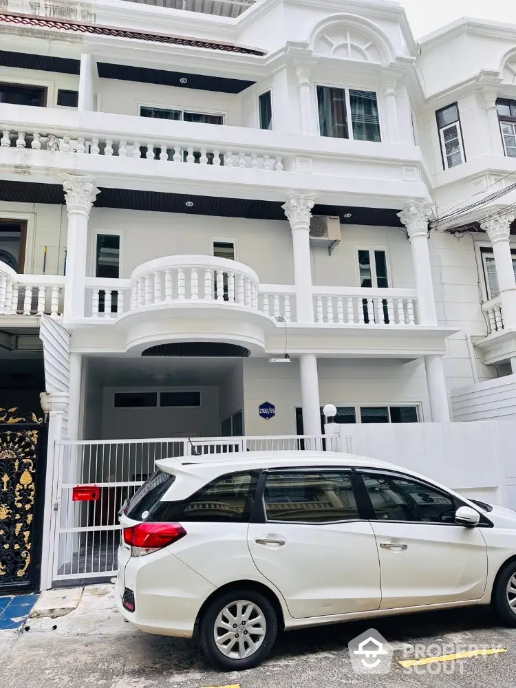 Elegant white townhouse with classic columns and balcony, featuring a parked car in front.