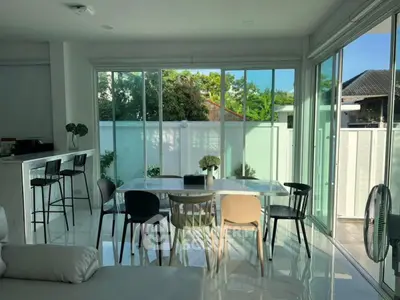 Modern dining area with glass walls and garden view, featuring sleek furniture and abundant natural light.