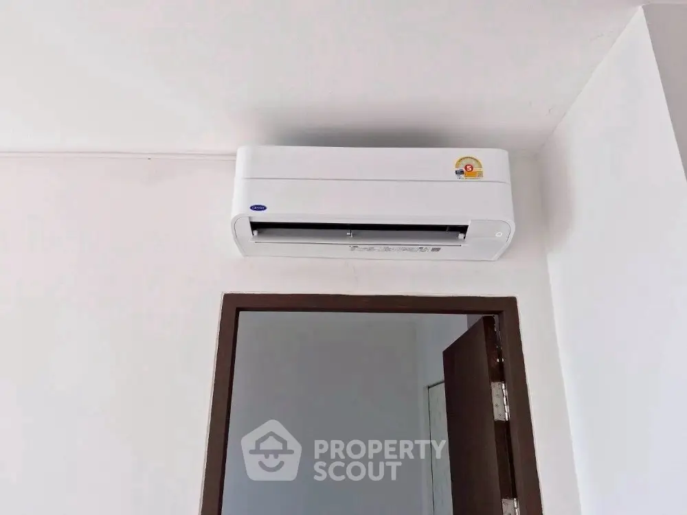 Modern air conditioning unit installed above a door in a minimalist interior space.