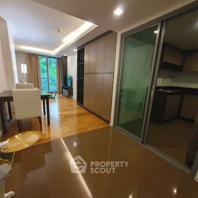 Modern living room with open layout and sleek kitchen design, featuring hardwood floors and large windows.