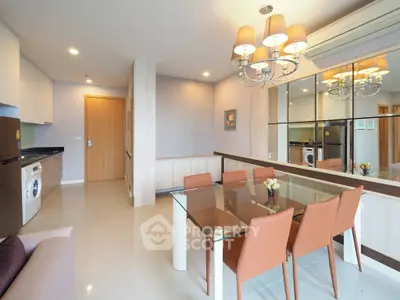 Modern dining area with glass table, stylish chairs, and mirrored wall in open-plan apartment.