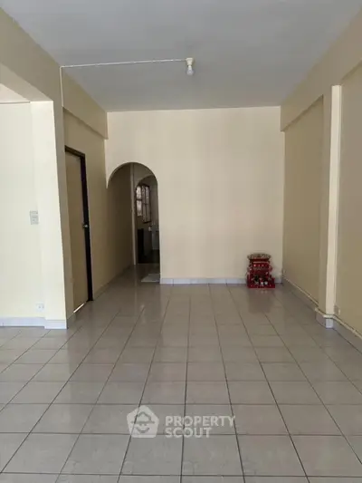 Spacious empty room with tiled flooring and archway entrance, ideal for customization.