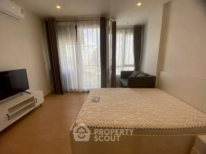 Modern bedroom with large windows and natural light, featuring a comfortable bed and cozy seating area.