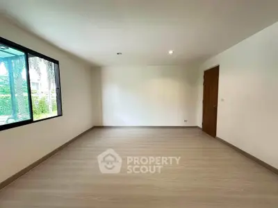 Spacious empty room with large window and wooden flooring, ideal for customization.