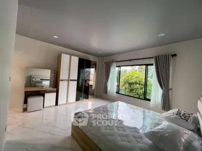 Spacious bedroom with large window and modern furnishings, offering a serene view of greenery.