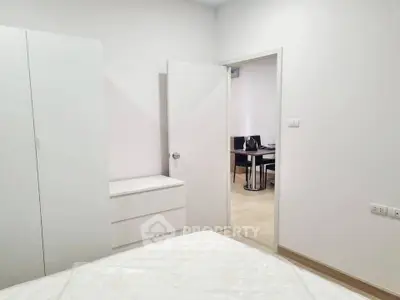Modern bedroom with white furniture and view into dining area, showcasing minimalist design.