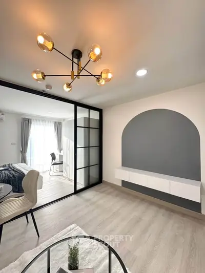 Modern living room with stylish chandelier and glass partition leading to bedroom.