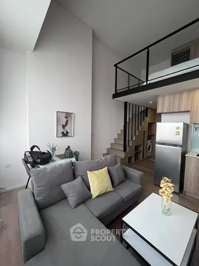 Modern loft apartment with stylish living room and kitchen, featuring a cozy gray sofa and sleek staircase.