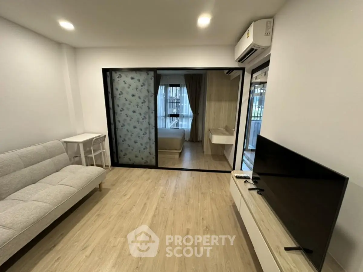 Modern living room with sleek design and large TV, featuring sliding glass doors to bedroom.