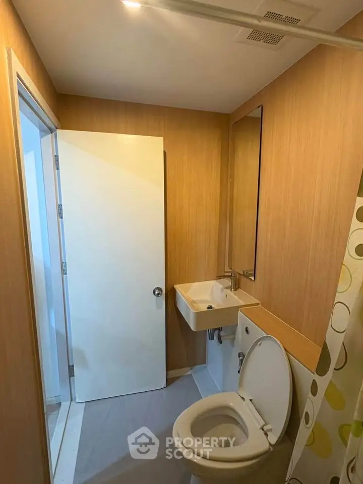 Compact bathroom with modern fixtures and wooden paneling, featuring a toilet and sink.