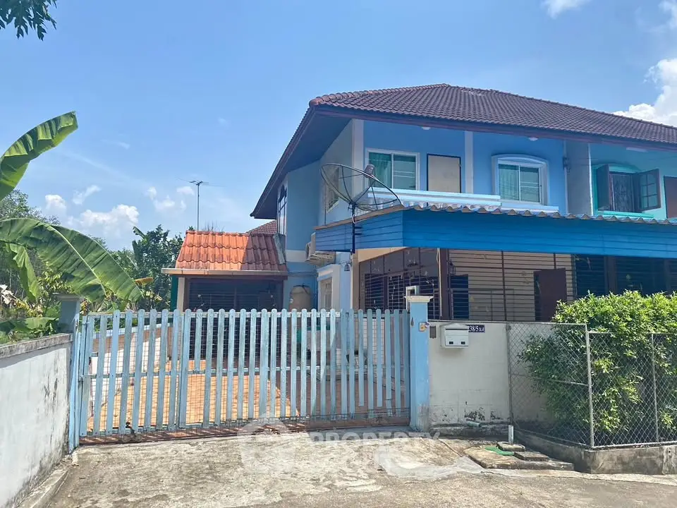 Charming blue two-story house with gated entrance and lush greenery.