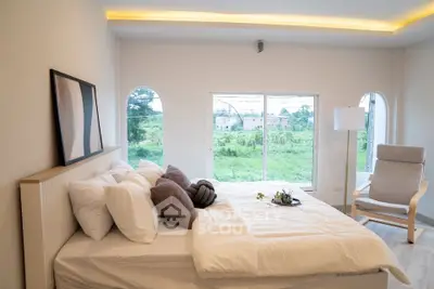 Spacious bedroom with large window offering serene green views, modern decor, and cozy ambiance.
