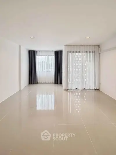 Spacious empty living room with large windows and elegant curtains.