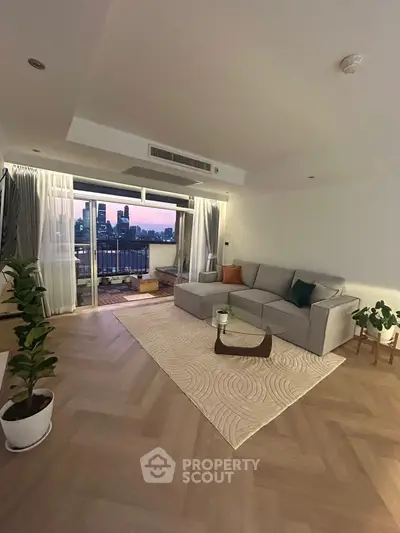 Spacious living room with modern decor and city view balcony at sunset.