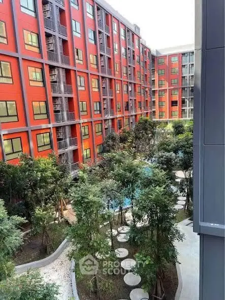 Modern apartment complex with lush garden courtyard and vibrant red facade.