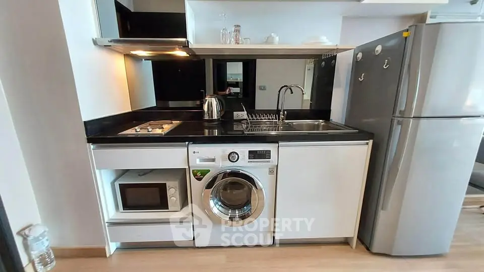 Modern compact kitchen with washing machine, microwave, and fridge in sleek apartment.
