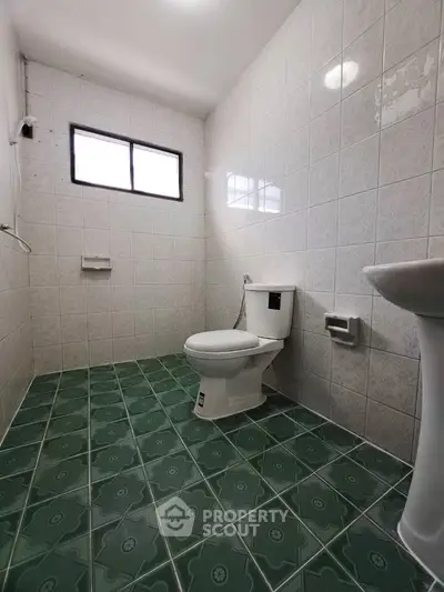 Spacious bathroom with green tiled floor and white fixtures, offering a clean and simple design.