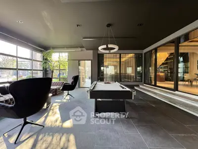 Luxurious modern living space with pool table and large windows offering natural light and garden view.