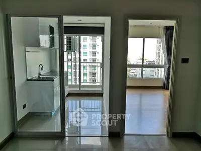 Modern apartment interior with sleek kitchen and bright living area, featuring large windows and balcony access.