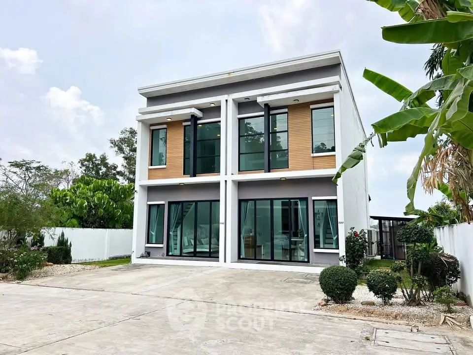 Modern two-story house with large windows and lush greenery, perfect for contemporary living.