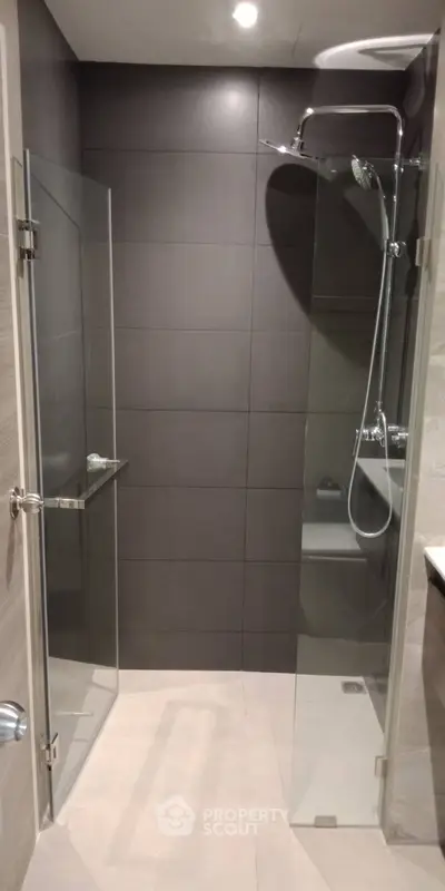 Modern bathroom with sleek glass shower enclosure and dark tile walls.