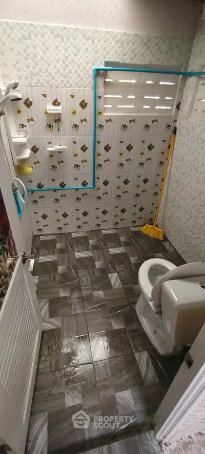 Compact bathroom with tiled walls and floor, featuring a toilet and cleaning supplies.