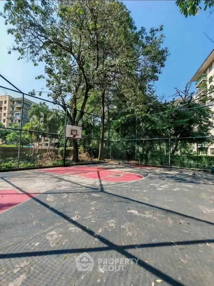 Outdoor basketball court surrounded by lush greenery in a residential complex.