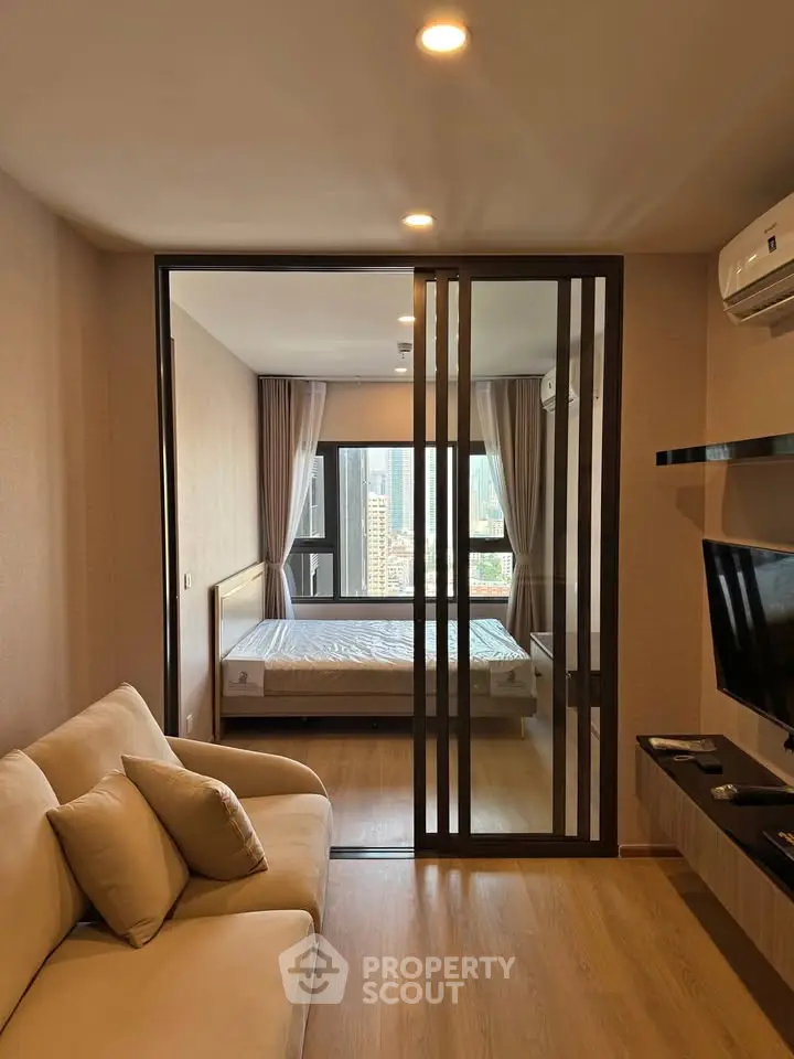 Modern apartment with sliding glass doors separating living room and bedroom, featuring city views.