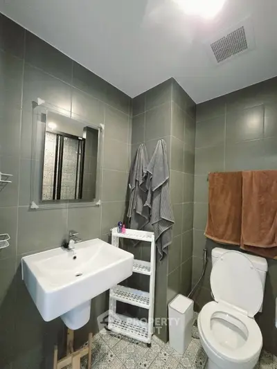 Modern bathroom with sleek gray tiles and stylish fixtures, featuring a spacious sink and elegant towel arrangement.