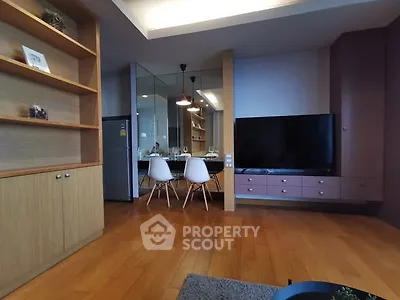 Modern living room with wooden flooring and large TV, open dining area with stylish chairs.