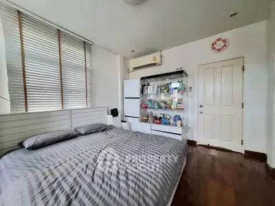 Cozy bedroom with striped bedding, wooden floor, and ample natural light from large windows.
