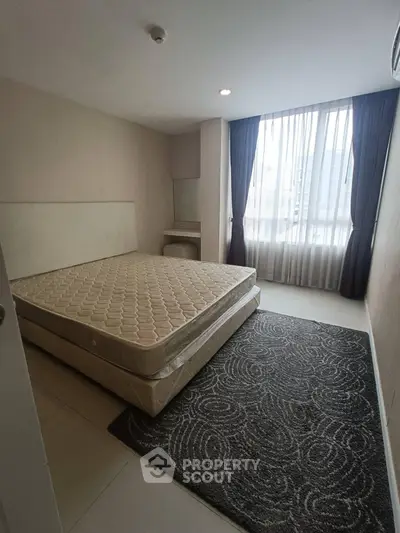 Spacious bedroom with large window and natural light in modern apartment.