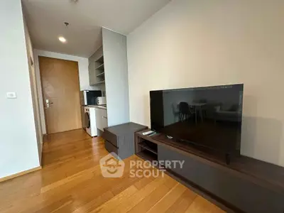 Modern living room with wooden flooring, TV, and compact kitchen area in a stylish apartment.