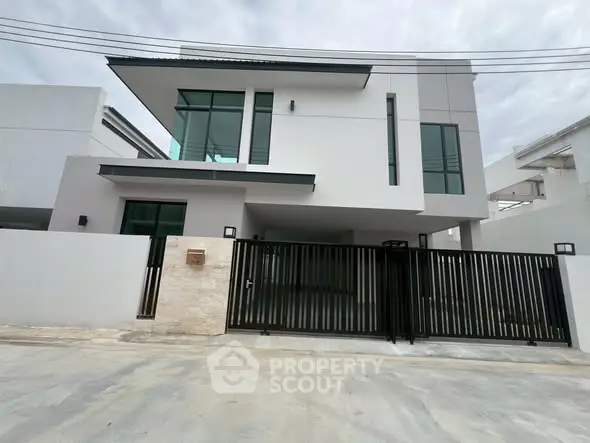 Modern two-story house with sleek design and large windows, featuring a gated entrance and contemporary architecture.
