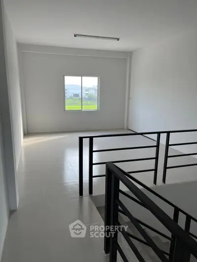 Spacious modern interior with large window and sleek railing, perfect for natural light and open living.