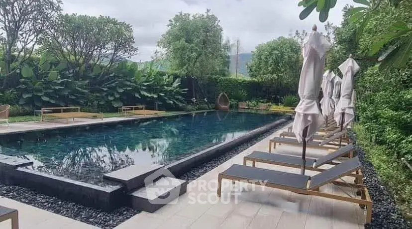 Luxurious outdoor pool area with lush greenery and elegant sun loungers, perfect for relaxation and leisure.