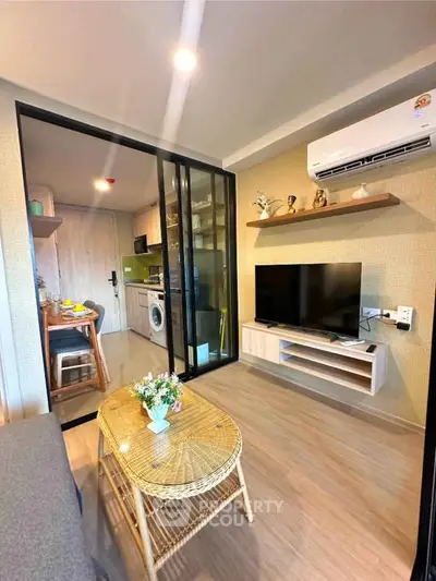 Modern living room with open kitchen, featuring TV, air conditioning, and stylish decor.