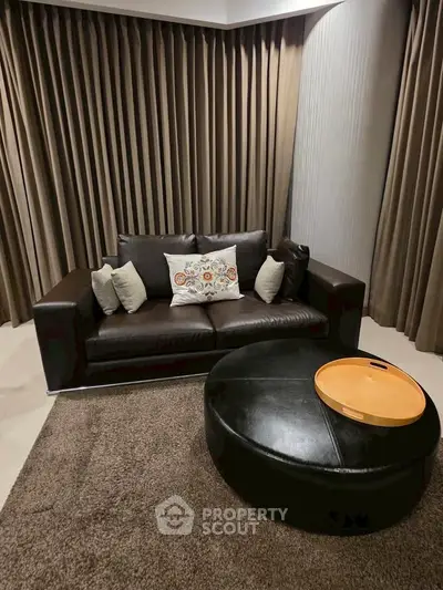 Cozy living room with dark leather sofa and round ottoman, perfect for relaxation.