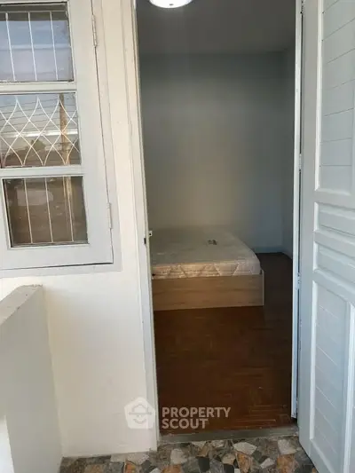 Cozy bedroom with parquet flooring and natural light from window, perfect for relaxation.