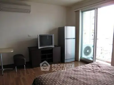 Cozy bedroom with balcony access, featuring a TV and fridge, ideal for modern living.