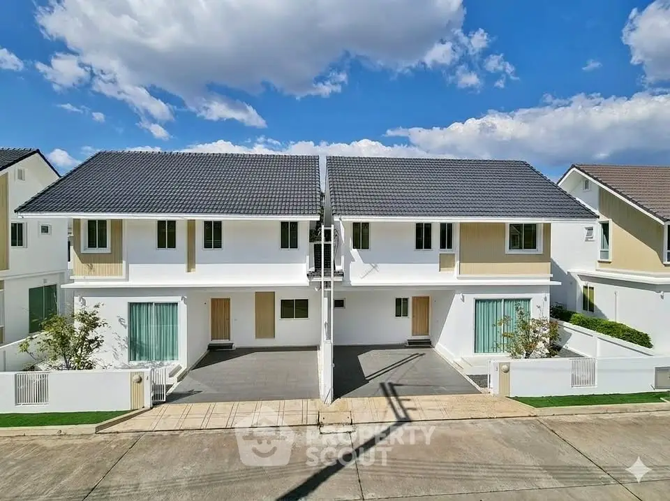 Modern duplex homes with sleek design and spacious driveways under a clear blue sky.
