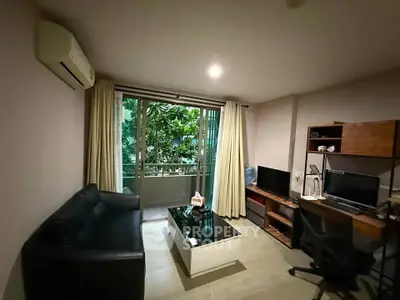 Modern living room with balcony view, featuring sleek furniture and a home office setup.