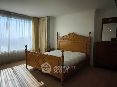 Spacious bedroom with elegant wooden furniture and large window with natural light.