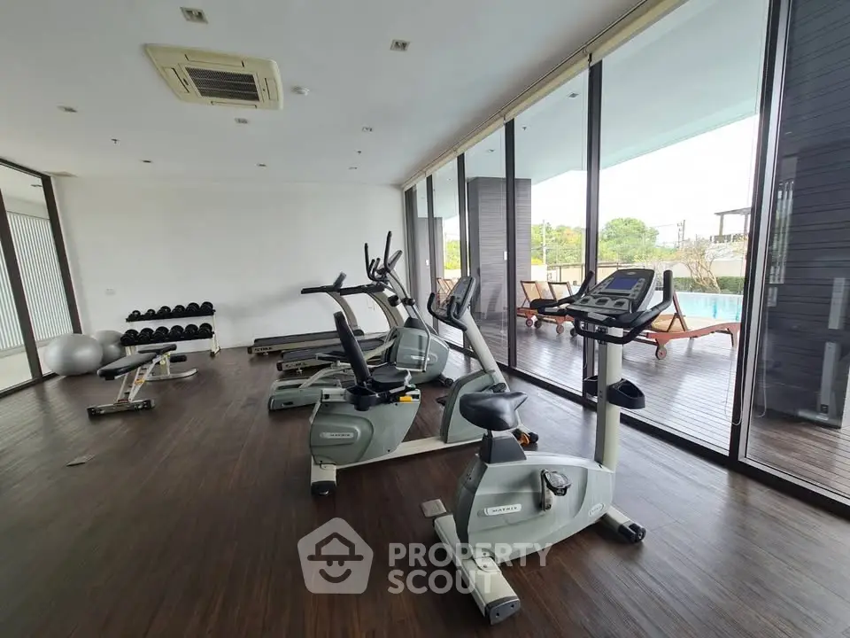 Modern gym with exercise equipment and pool view in luxury apartment complex.