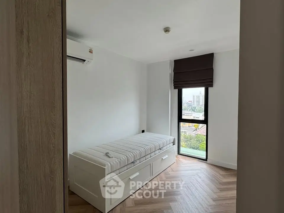 Cozy bedroom with single bed and city view window, perfect for urban living.